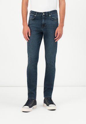 Dark blue denim jeans with a classic fit, featuring five pockets, subtle fading, and a straight leg design. Paired with black sneakers.