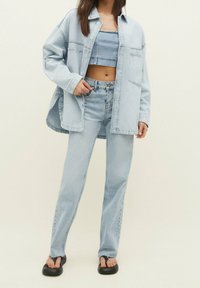 Helles blaues Denim-Outfit bestehend aus einem cropped Top, einem oversized Hemd und geraden Jeans. Merkmale sind eine glatte Textur und subtile Nähte.