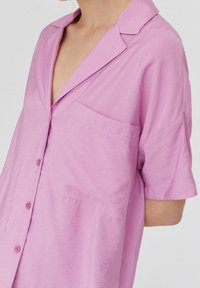 Camisa de manga corta rosa claro, con botones en el frente, cuello con solapa, un bolsillo en el pecho, tejido suave, corte relajado, textura lisa.