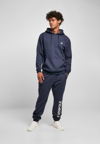 Navy sweatshirt with a hood and front pocket, paired with matching jogger pants featuring a white logo print on the leg.