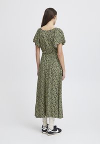 Floral maxi dress in dark green with short, ruffled sleeves. Features a fitted waist and flowing skirt. Paired with black sneakers and cream socks.