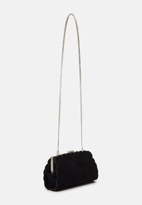 Black suede handbag with a scalloped design. Features a silver chain strap and a clasp closure, with a smooth texture and structured shape.