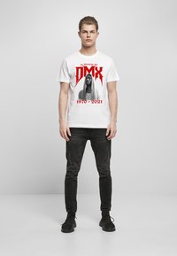 Hvit bomulls t-skjorte med trykk i svart og rødt av DMX med teksten "In Memory Of" og årene "1970 - 2021." Kombinert med svarte jeans.