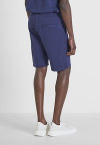 Pantaloni corti blu navy realizzati in tessuto morbido, con tasche laterali e una tasca sul retro. Abbinati a sneaker bianche.