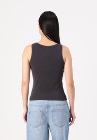 Top cinza sem mangas com decote redondo e corte justo, combinado com jeans de cintura alta azul claro com bolsos traseiros e estilo casual.