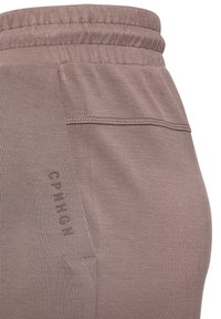 Detailný záber na levanduľovo fialové nohavice z látky, zobrazujúce elastický pás, bočnú kapsu s vertikálnymšvovým stehom a text "CPNHGN" pozdĺž okraja kapsy.