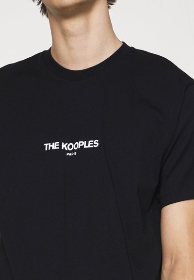 Svart bomull T-skjorte med rund hals, med hvit tekst som leser "THE KOOPLES PARIS" sentrert på brystet. Enkelt design og glatt tekstur.