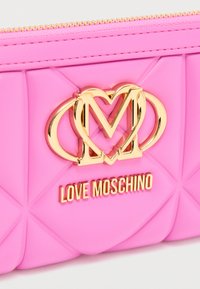 Ροζ πορτοφόλι από συνθετικό δέρμα με καπιτονέ σχέδιο, εξαρτήματα σε χρυσό τόνο και ανάγλυφο λογότυπο "LOVE MOSCHINO" με διαπλεκόμενες καρδιές.