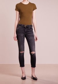 Oliwkowa dopasowana koszulka, ciemnoniebieskie wytarte skinny jeansy z przetarciami na kolanach, srebrny pasek z klamrą, zestawione z czarnymi balerinami.