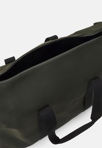 Tamnozeleni torba na remen s glatkom, mat teksturom, s dva čvrsta ručka i gornjim zatvaračem. Unutrašnjost je crna.