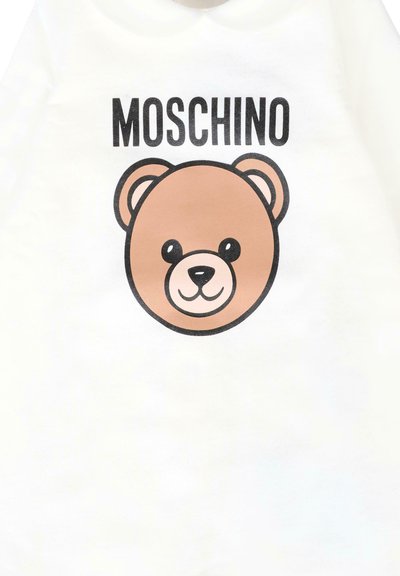Biała bawełniana koszula z brązową, rysunkową twarzą misia z uśmiechniętym wyrazem twarzy oraz napisem "MOSCHINO" powyżej, napisanym dużymi, czarnymi literami.