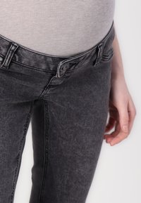 Jeans de mezclilla gris oscuro con una cintura alta, con cierre de botón y trabillas para cinturón. Textura suave con ligeros desgastes y detalles de costura.