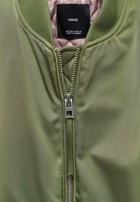 Olivgrüne Bomberjacke mit einem Reißverschluss, geripptem Kragen und wattierter Fütterung. Verfügt über ein Markenetikett auf der Innenseite.