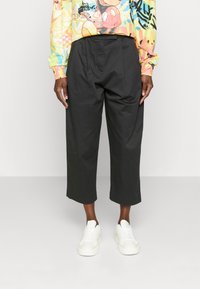 Černé zkrácené kalhoty s záhyby, vyrobené z hladké tkaniny. V kombinaci s bílými teniskami. Košile má barevné grafické vzory.