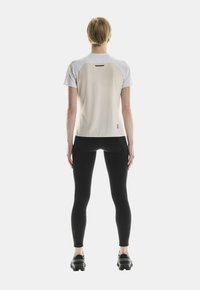 T-shirt de sport léger, devant crème, dos gris, manches courtes, tissu texturé, associé à des leggings noirs et des chaussures de sport.