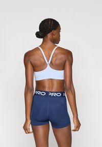 Ανοιχτό μπλε αθλητικό σουτιέν με σχεδίαση racerback, σε συνδυασμό με σκούρο μπλε σορτς που έχει εμφανές λευκό λογότυπο στη μέση.