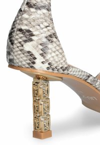 Sandalo con tacco alto, con una tomaia in stampa serpente beige e nera testurizzata, dotato di un tacco a blocco dorato con un design geometrico e base solida.