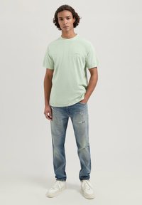 Lys grønne kortermede t-skjorte med rund hals, kombinert med slitte blå jeans og hvite joggesko. Glatt stoff og avslappet passform.