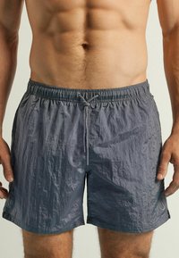 Grijze zwembroek van lichtgewicht, gestructureerde stof. Voorzien van een elastische tailleband met trekkoord, zijzakken en een klein logo-accent.