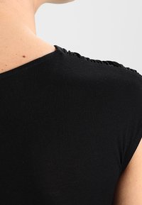 T-shirt nero aderente con scollatura rotonda. Il tessuto è morbido ed elastico, con dettagli arricciati lungo la cucitura della spalla.