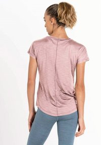 Top atlético rosa claro con mangas cortas, dobladillo redondeado y detalle de costura en la parte posterior, combinado con leggings azul claro. Textura suave.