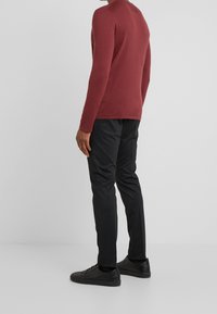 Chemise en maille bordeaux à manches longues associée à un pantalon noir ajusté et des baskets noires. Texture lisse avec une silhouette ajustée.