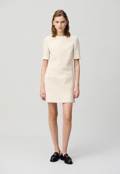 Robe crème à manches courtes, en tissu texturé, avec un design ajusté et deux poches à l'avant. Associée à des mocassins noirs.