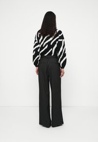 Pull rayé noir et blanc avec une texture duveteuse, associé à un pantalon noir taille haute à fines rayures blanches et jambes larges.