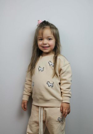 Beige sweatshirt en bijpassende broek met geborduurde hondontwerpen. Zachte katoenen stof met lange mouwen en een tailleband met trekkoord.