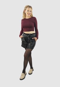 Bordeaux gekleurde lange mouwen cropped top, zwarte neplederen shorts met ruches aan de taille, zwarte panty met stippen, lichtbeige loafers met gouden accenten.