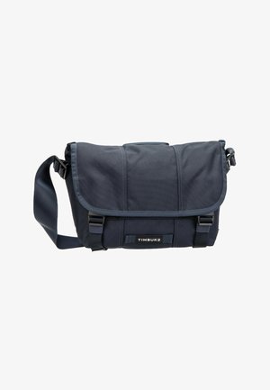 Marineblaue Timbuk2-Umhängetasche mit verstellbarem Schulterriemen, Frontklappe, zwei Schnallenverschlüssen und sichtbarem Markenlabel.