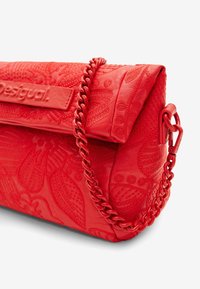 Czerwona torebka skórzana z wytłoczonym kwiatowym wzorem, z klapą składana oraz masywnym łańcuchem na pasku. Logo widoczne z przodu.
