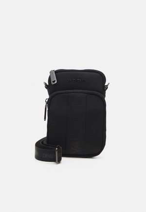 Sac en nylon noir à bandoulière avec fermeture éclair, logo texturé à l'avant et une sangle réglable avec branding. Finition lisse sur l'ensemble.