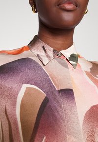 Chemise boutonnée en tissu léger présentant un motif abstrait aquarelle aux nuances de marron, orange et violet ; détail col classique.