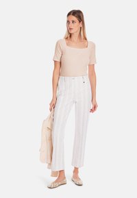 Beige fitted top with square neckline, white pants featuring a leafy print, and tan shoes. Holding a light-colored blazer.