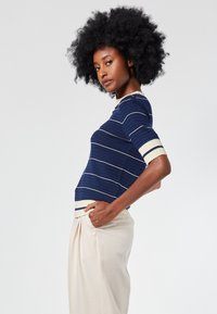 Navy blue short-sleeve knit top with white stripes and textured fabric. Features a ribbed crew neck and a contrasting beige hem.