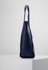 Laivastonsininen nahkalaukku, jossa on kiiltävä pinta, tyylikäs muotoilu ja pitkä muoto. Siinä on kaksi yläkahvaa ja kontrastivärinen reunus.