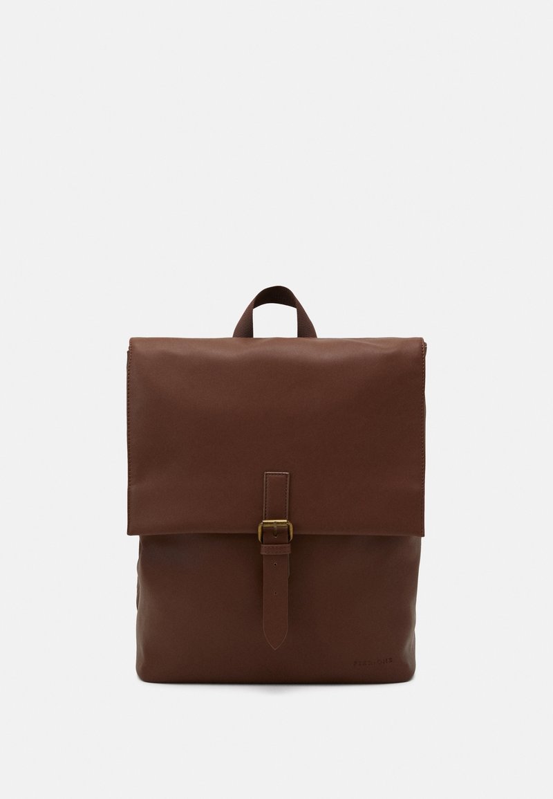 Un sac à dos en cuir marron avec un rabat de fermeture, une sangle à boucle et une poignée supérieure. Texture lisse, design simple et sans motifs visibles.