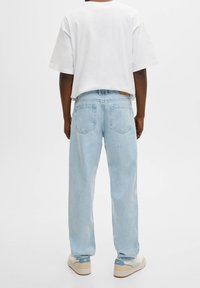 Jeans de mezclilla azul claro con un corte relajado, que cuentan con doble bolsillo trasero. Combinados con una camiseta blanca básica de gran tamaño y zapatillas beige.