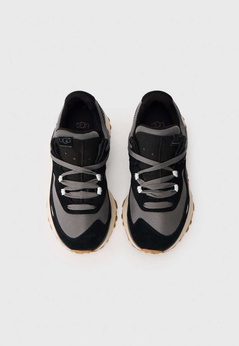 Chaussures de sport noires et grises en matériaux en maille et en daim, avec un design distinctif, des lacets ronds et une semelle en caoutchouc beige.