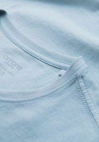 Světle modré bavlněné tričko s kulatým výstřihem. Obsahuje žebrovaný límeček a detaily prošívání. Na štítku je značka "ombre".
