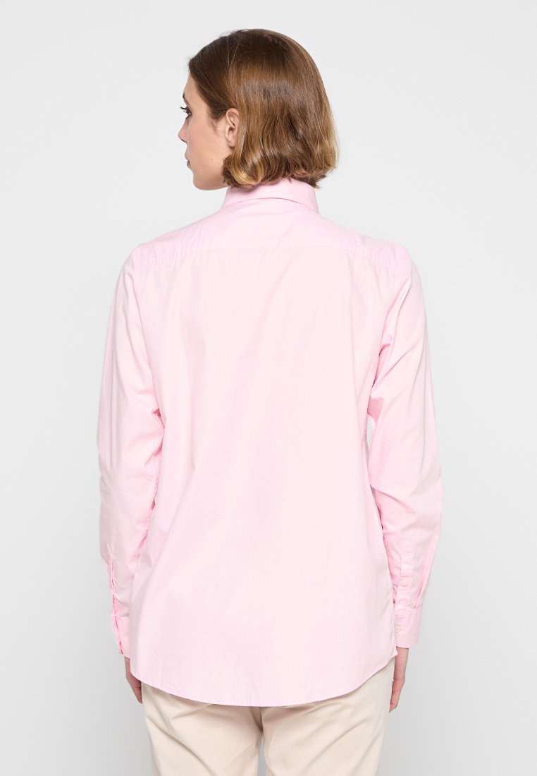 Chemise boutonnée rose clair à manches longues, avec un col pointu et un ourlet arrondi. Fabriquée dans un tissu léger et doux ; elle possède un empiècement au dos.