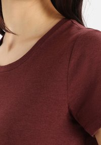 Burgundské tričko s kulatým výstřihem a krátkými rukávy. Hladká bavlněná tkanina s mírně měkkou texturou a minimálními švy na ramenech.