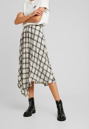 Jupe midi à carreaux avec un ourlet asymétrique en crème, noir et rouille. Tissu léger avec des plis ; portée avec des bottes de combat noires.