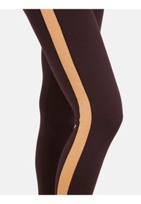 Bruine leggings met een contrasterende lichtbruine verticale streep aan de buitenkant, gemaakt van een zachte, rekbare stof.