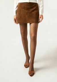 Mini jupe en daim marron associée à des collants marron à motifs en losange et des chaussures à talons ouverts marron, mettant en valeur les textures et les détails de design.