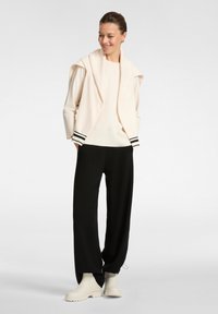 Top crema con vestibilità comoda, spalle scese e dettagli a strisce nere. Pantaloni neri larghi e stivali beige completano l'outfit.