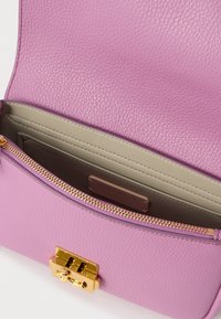 Borsa in pelle rosa con superficie texturizzata, dettagli in oro e chiusura con zip. L'interno presenta scomparti neutri e un'etichetta del marchio.