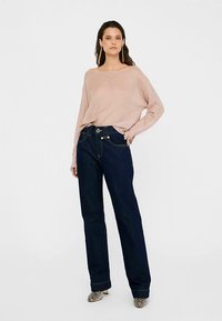 Gaiši rozā ribots džemperis ar platu kakla izgriezumu, kopā ar tumši zilām, augsta vidukļa džinsu biksēm ar zelta detaļām un sānu kabatām.