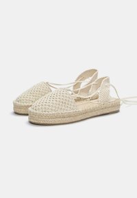 Espadrilles en crochet beige avec un bout rond, une tige tissée et un arrière à lacets. Elles disposent d'une semelle en jute tissée et d'un tissu texturé pour une meilleure adhérence.